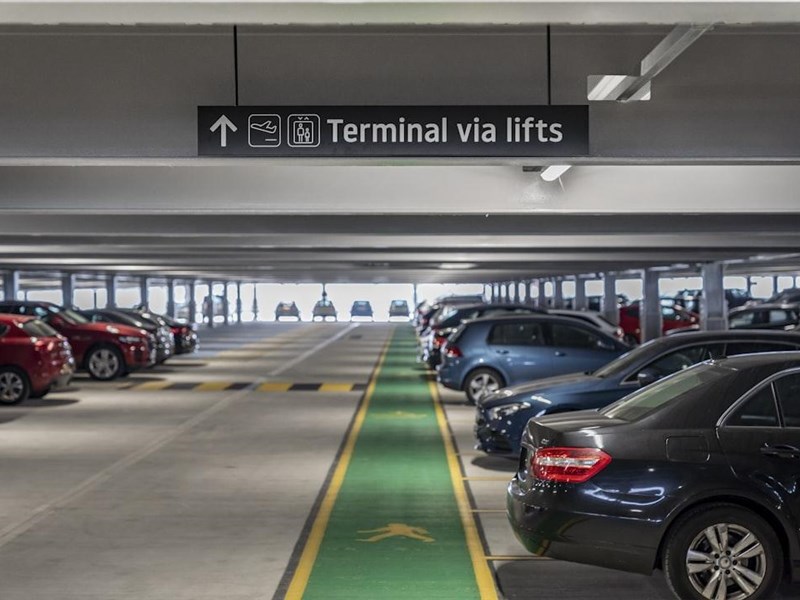 Cars in an airport car park with an aircraft in the background
